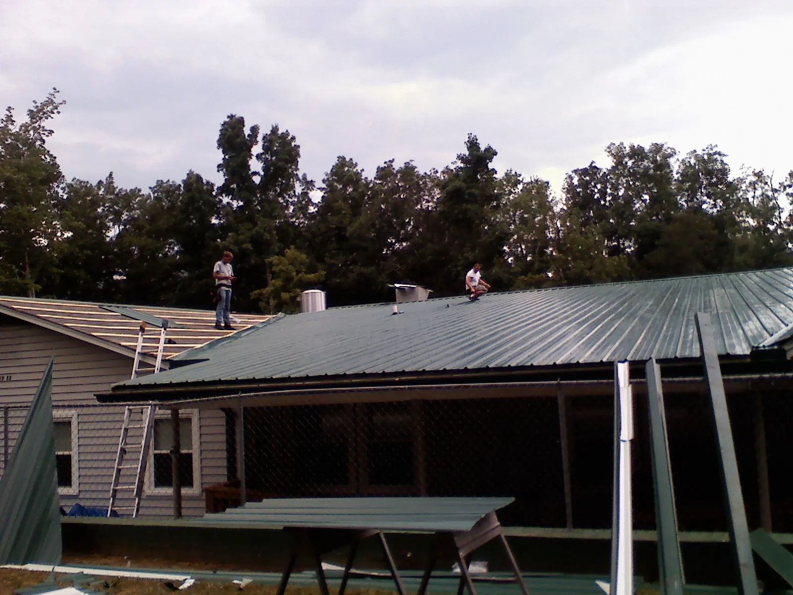 Two roofers installing green metal panels above a covered porch in Wakefield