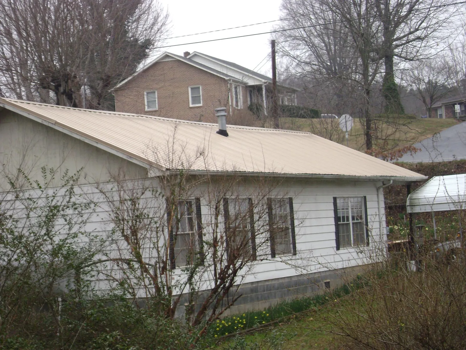 Tan metal roof on a white sided house set into a hillside — Commercial Roofing by Roofing Brothers in Wakefield